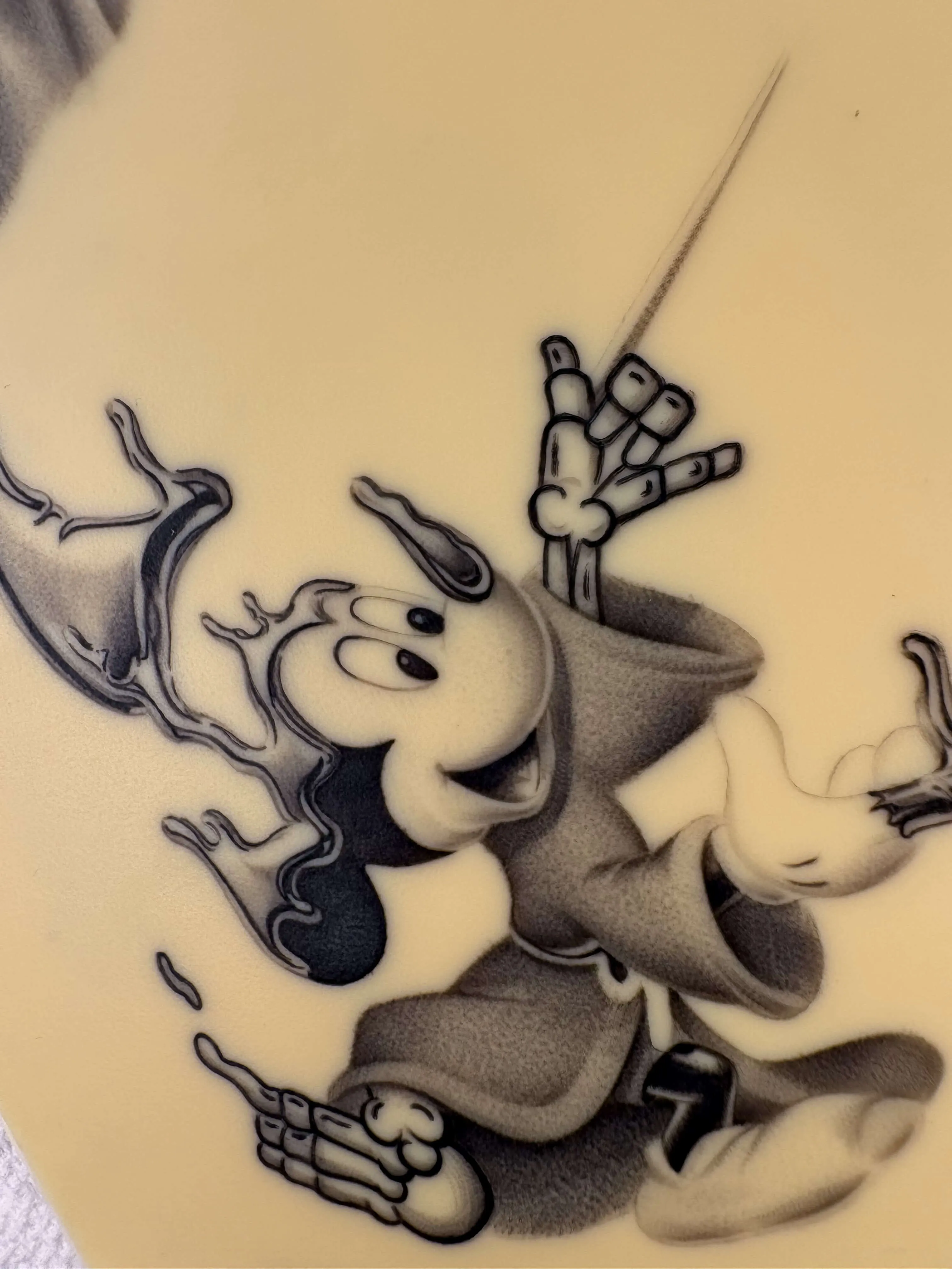Close-up of black and grey fine line tattoo on practice skin featuring melting Sorcerer Mickey with skeleton hands
